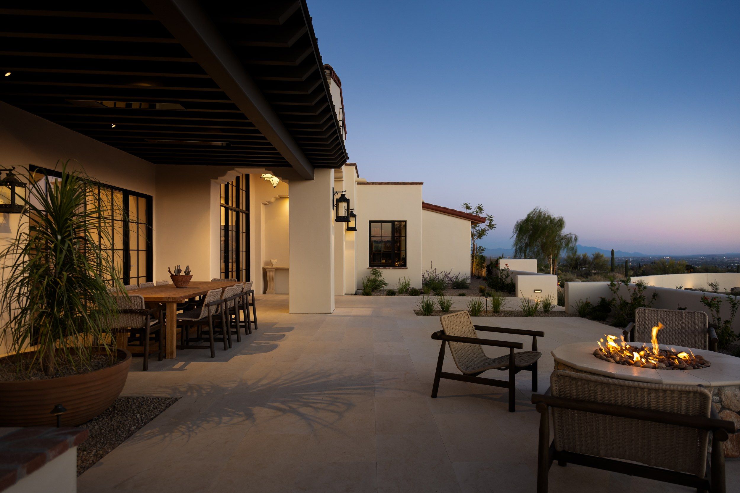Covered terrace at dusk with a dining table and a lit fire feature