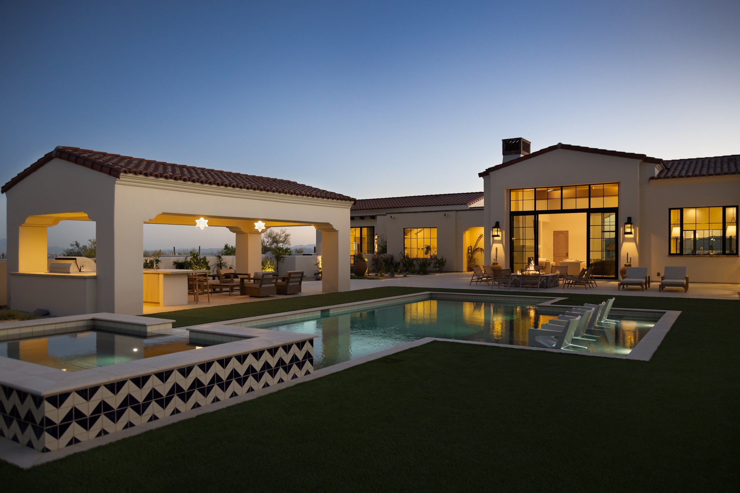 Pool and spa lit at dusk with the ramada and house glowing