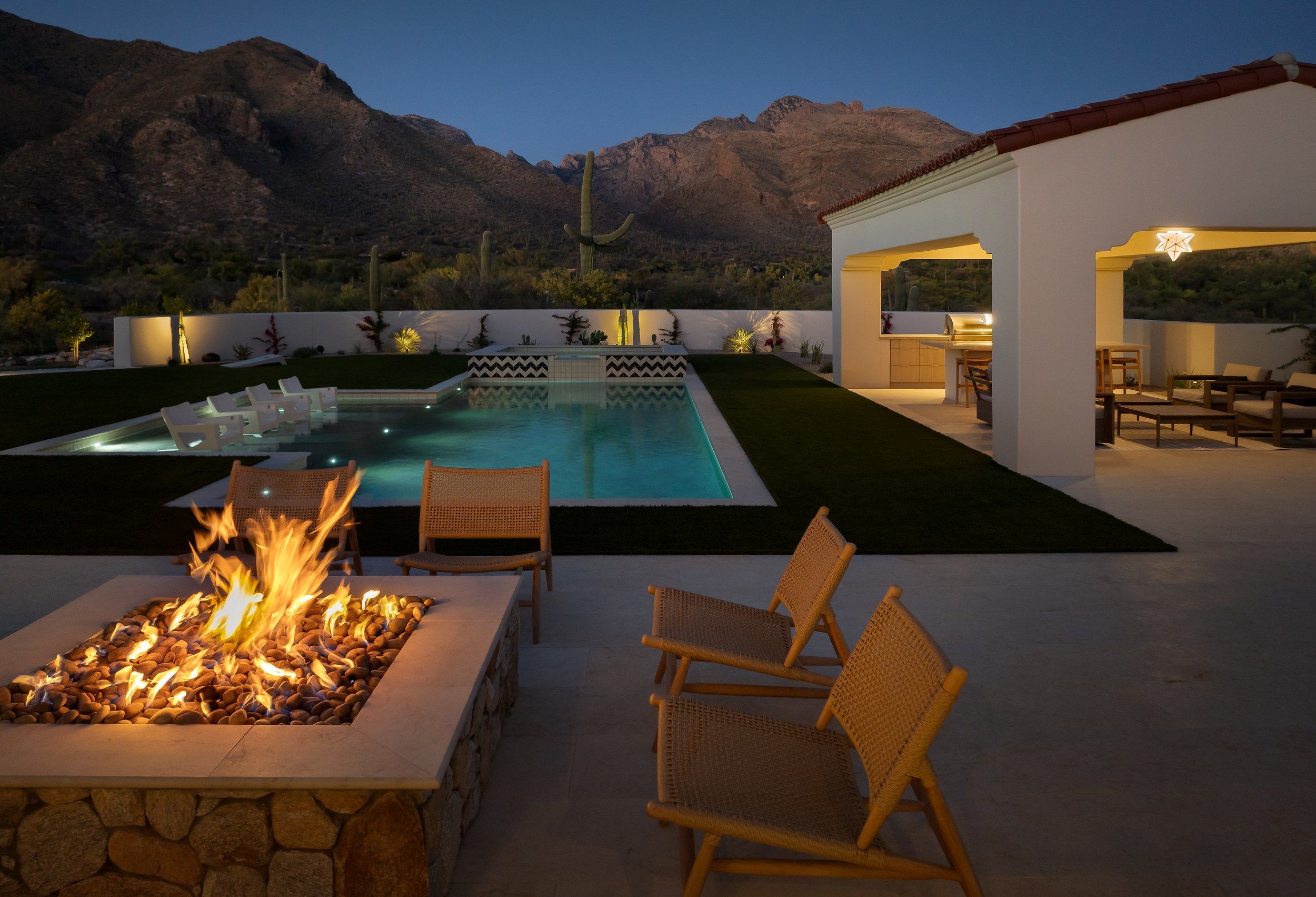 Fire table beside the lit pool at twilight with the mountains beyond